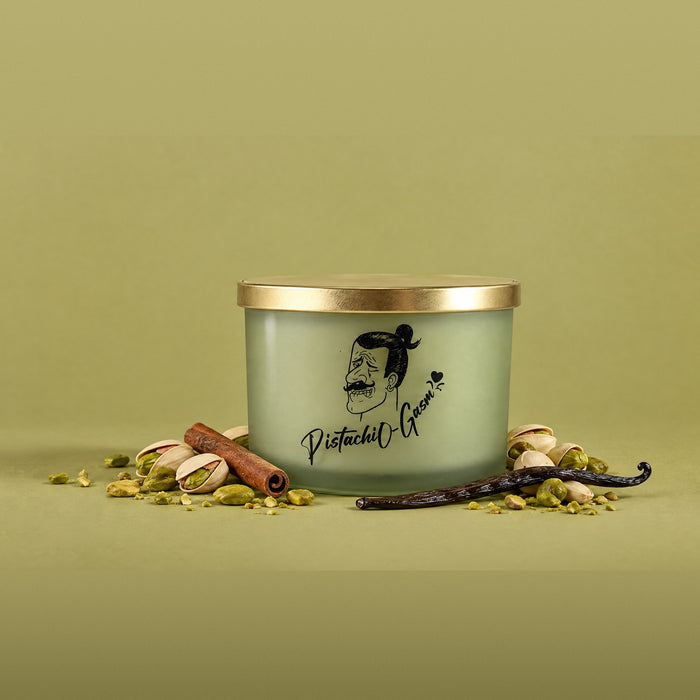 Pistachiogasm soy candle with a gold lid, surrounded by pistachios, cinnamon and vanilla